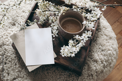 Spring still life composition. Greeting card mockup, cup of coffee. Feminine styled photo. Floral scene with blurred white cherry tree blossoms on wool taburet, stool. Wooden parquet floor. Selective