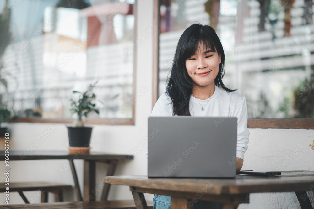 Young Asian woman with a pleasant smile engaging in online work on her laptop at a cozy cafe. Young Asian woman with a pleasant smile engaging in online work on her laptop at a cozy cafe.