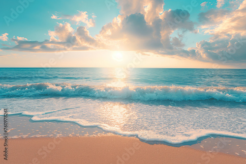 Sunset over the sea with waves touching the sandy beach, reflecting the sun's light under a clouded sky.