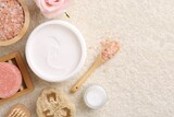 Flat lay composition with moisturizing cream in open jar and other body care products on light textured table. Space for text
