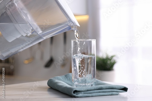Pouring water from filter jug into glass in kitchen, closeup photo