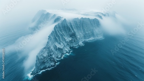 Dramatic aerial view of a foggy mountain range descending into the sea, with cascading mist creating a seamless transition between the rugged terrain and the ocean's expanse © Ross