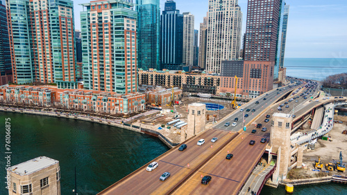  An aerial drone  view of a bustling Chicago metropolis The cityscape is reflected in the serene waters of a green-tinted river. Cars stream along the adjacent highway