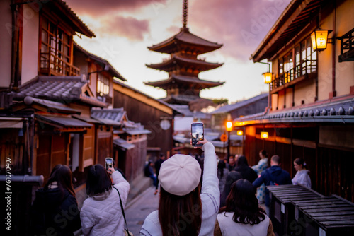 Yasaka Pagoda view and Hokan-ji Temple from Yasaka Dori street in Kyoto, Japan. Popular touristic street leading to Kyomizu Dera,Young female tourist taking photo with a mobile phone during sunset.