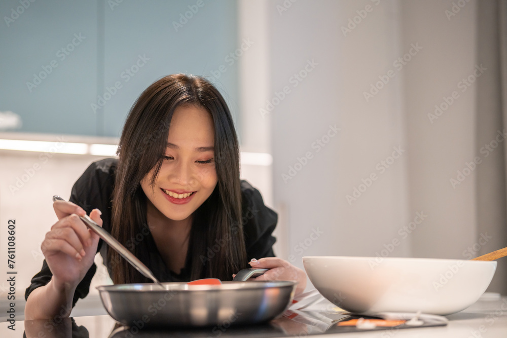 Young woman standing near stove and cooking, housewife, meal, chef, food.Happy woman looking and smelling tasting fresh delicious from soup in a pot with steam at white interior kitchen Young woman standing near stove and cooking, housewife, meal, chef, food.Happy woman looking and smelling tasting fresh delicious from soup in a pot with steam at white interior kitchen