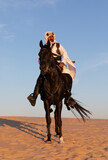 Saudi man in traditional clothing in a desert riding his black stallion