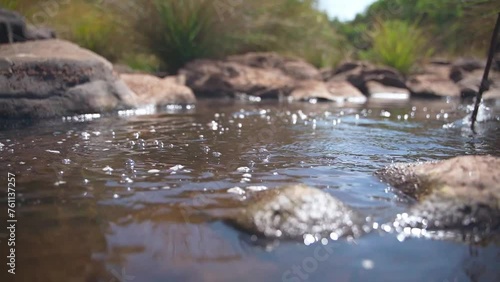 The girl runs a stick through the water, against the background of stones.