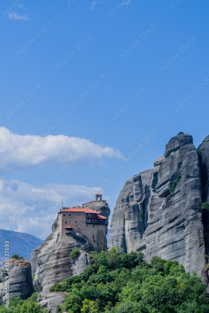 Vertical view of a monastery atop a monolithic rock with clear blue skies, in Meteora, Greece