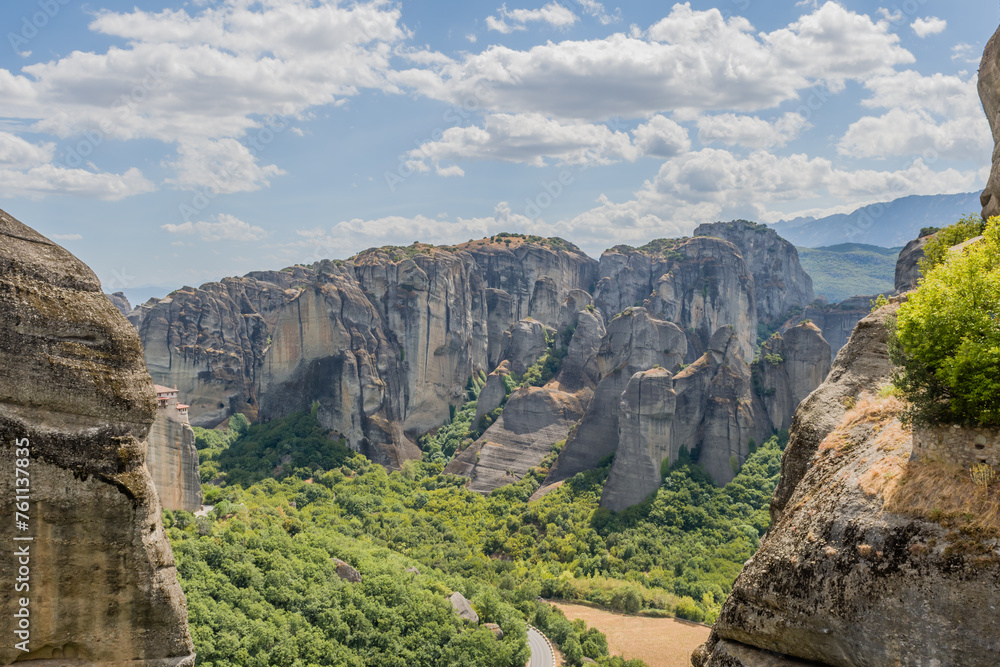 Fototapeta premium Panoramic view of Meteora's rock formations and valleys with lush greenery under a blue sky, in Meteora, Greece