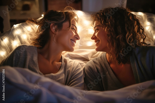 Two women, a couple, laying side by side in bed, exuding love and intimacy as they share a tender moment together