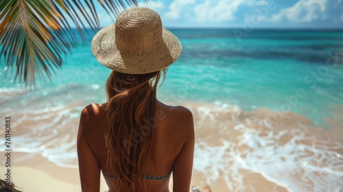 young blonde woman sitting at the beach overlooking the ocean - back view - travel concept