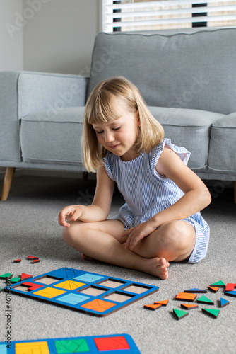 A cute girl is playing a logical wooden game on the floor in the room. Educational toy. 