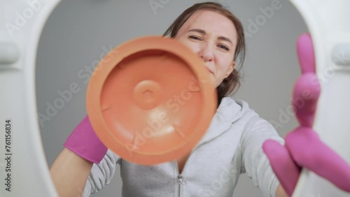 Woman plumber or homeowner is disgusted when cleaning clogged toilet using plunger. View from toilet bottom. Cleanliness and hygiene concept