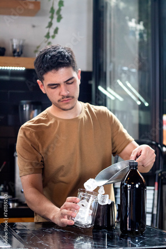 young barista pours ice into glass with small scoop