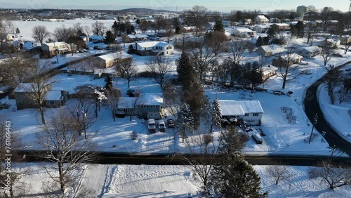 Snow covered homes and buildings in suburbia of american town in winter snow. Snowy countryside farm fields in background. Sunny day on winter day in USA. Aerial lateral wide shot.