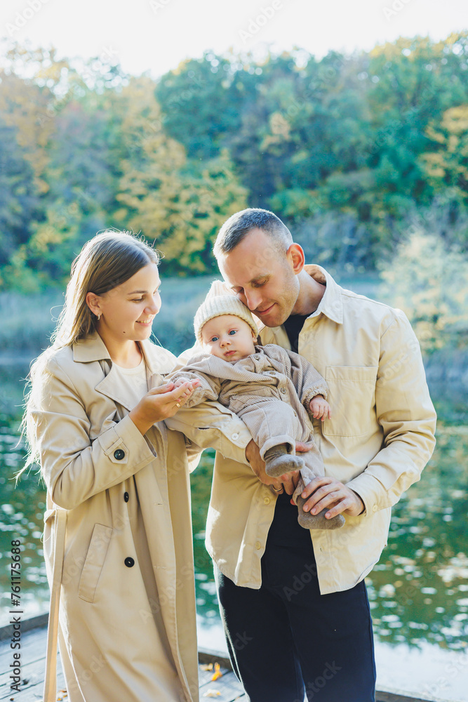 A happy young couple with a little son in their arms in the park near the lake. Family vacation in nature with a small son. The concept of family vacation. A happy young couple with a little son in their arms in the park near the lake. Family vacation in nature with a small son. The concept of family vacation.