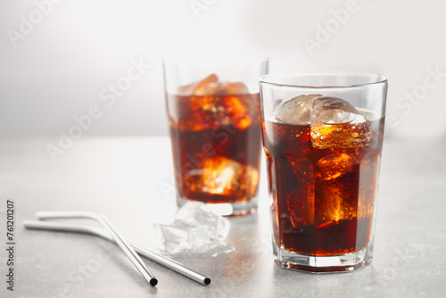 Two glasses of iced cola with ice cubes, with metal straws.