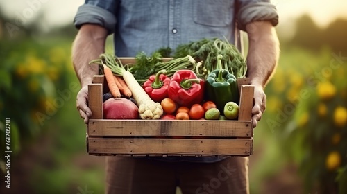 Farmer man holding wooden box full of fresh raw vegetables in his hands. Basket with vegetable in the hands.