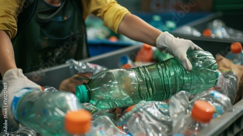 A worker with gloves on sorts through various plastic bottles, separating them for recycling in an industrial setting. © doraclub