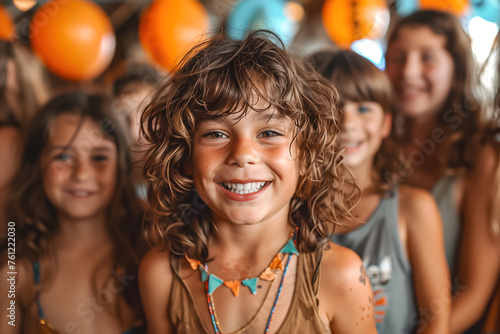 A curly-haired child beams joyfully at a party surrounded by friends and balloons, symbolizing happiness