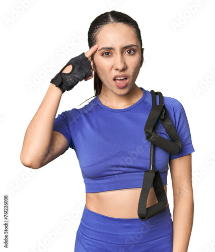 Athletic young Caucasian woman with resistance band on studio background showing a disappointment gesture with forefinger.