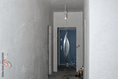 Prace wykończeniowe w nowym domu, zagruntowane ściany w korytarzu, wystająca elektryka w trakcie remontu