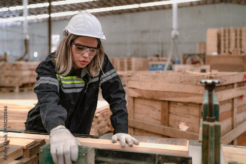 Confident worker woman standing in lumber warehouse of hardwood furniture factory inspecting production machine. Serious female technician, engineer busy working with tool in woodwork manufacturing.