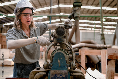 Confident female worker standing in lumber warehouse of hardwood furniture factory inspecting production machine. Serious technician woman, engineer busy working with tool in woodwork manufacturing.