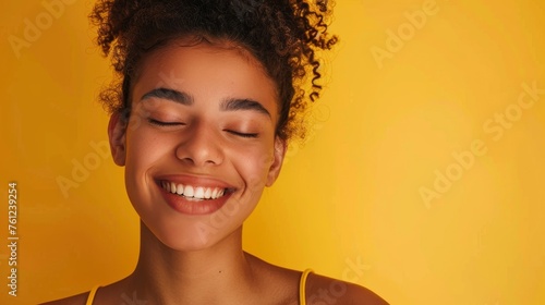 Photo with space for text. Portrait of an African American brunette girl with a smile and white teeth on a yellow background. Suitable for advertising