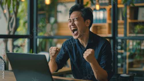 Ecstatic young man celebrating success at his laptop in a cafe.