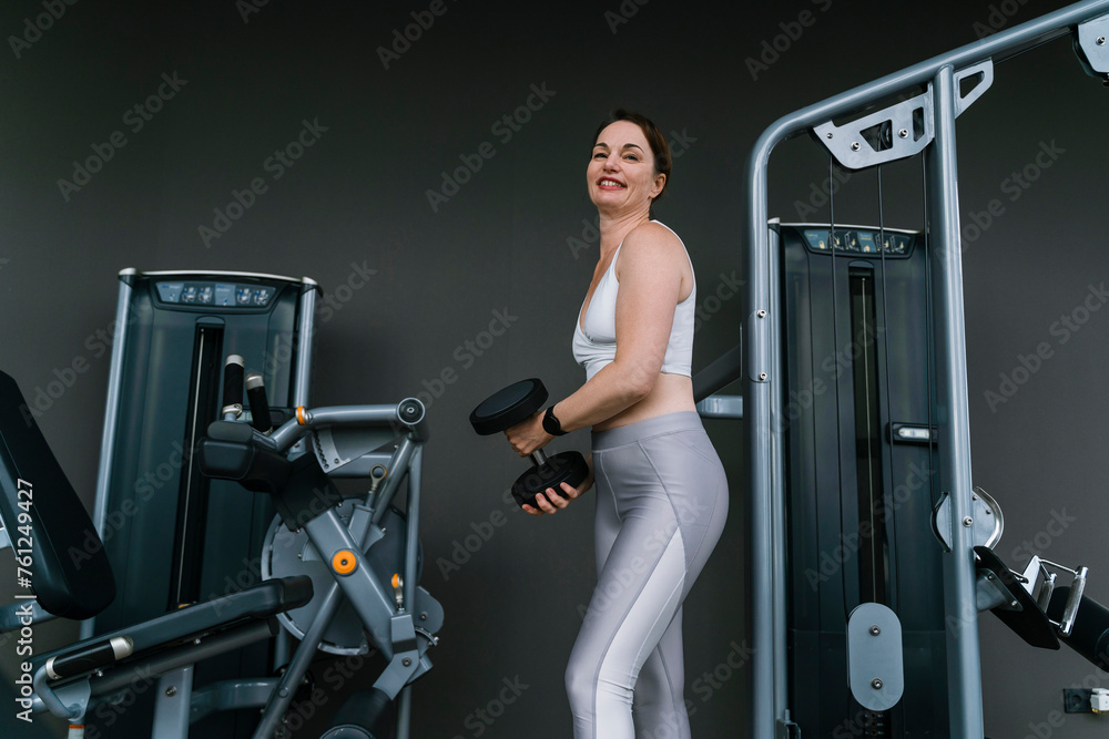 Happy woman doing weight training with dumbbell at gym Happy woman doing weight training with dumbbell at gym