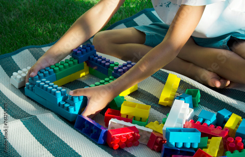 Boy 7 years old plays with plastic colorful blocks in garden on green grass. Sunset.