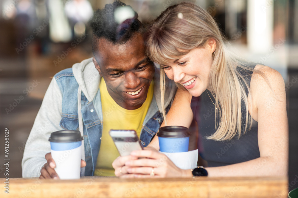 Excited friends sharing smart phone sitting at cafe Excited friends sharing smart phone sitting at cafe