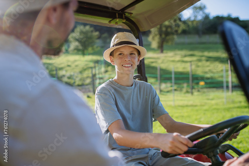 Farmer father letting his son drive the tractor. Boy growing up and working on family farm. Concept of multigenerational farming.