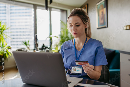 Nurse paying bills online with debit or credit card, working on notebook. Doctor in uniform shopping online, Work-life balance for healthcare worker. photo