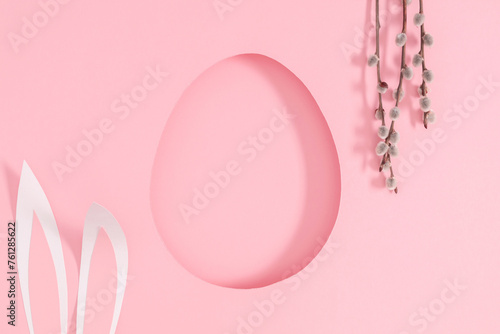 Happy Easter composition. Fluffy willow twigs  protruding bunny ears and an Easter egg shaped frame on pastel pink background.Top view. Flat lay.