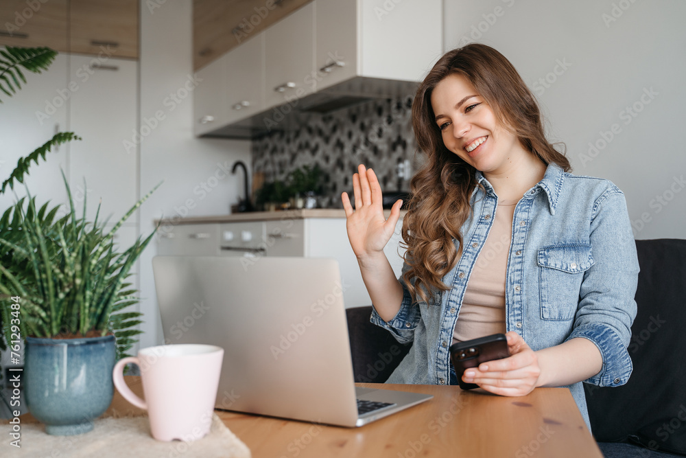 A woman sits at a table with laptop, cell phone, and houseplant, smiling A woman sits at a table with laptop, cell phone, and houseplant, smiling
