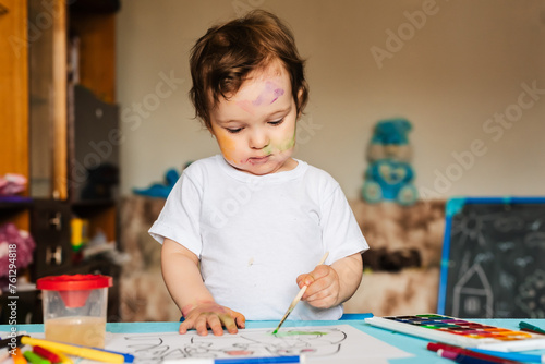 Happy cheerful child drawing with brush in album using a lot of painting tools.
