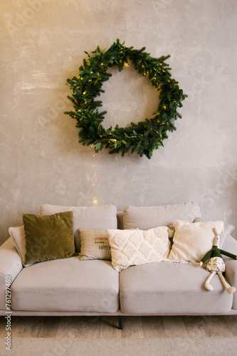 Interior design of the house with a sofa, pillows and a large fir wreath on the wall decorated for the new year