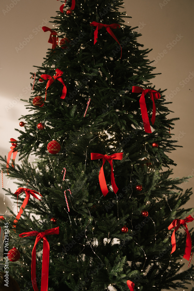 Beautiful New Year decor, the Christmas tree is decorated with red bows in the stylish interior of the living room