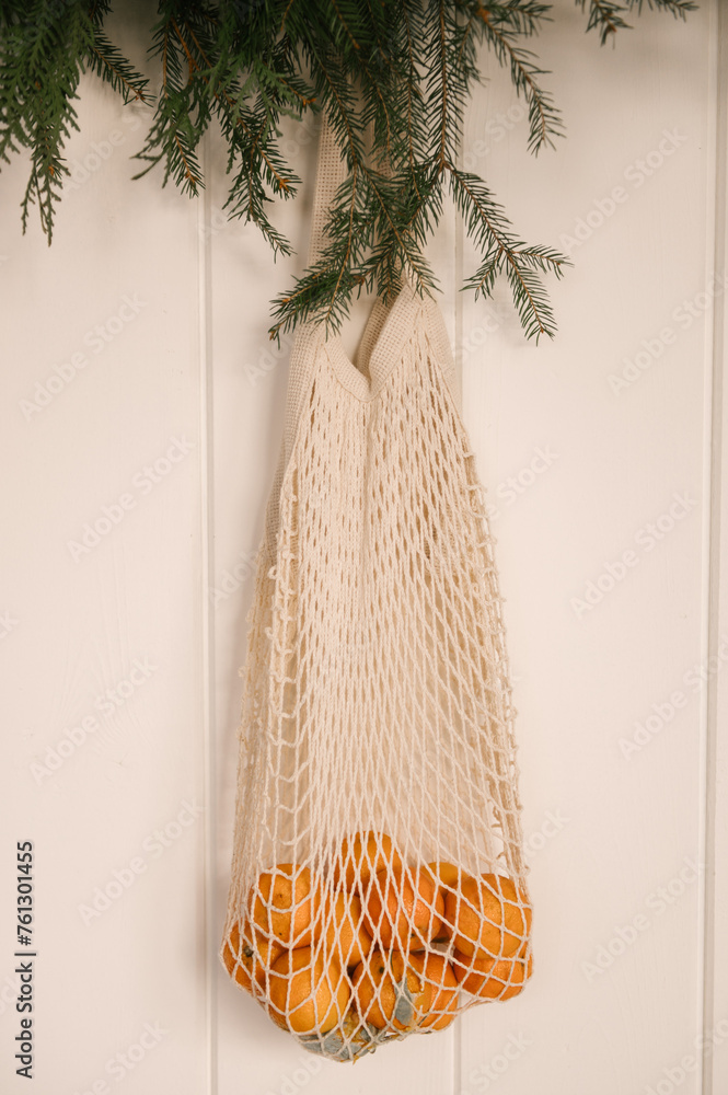Beautiful New Year decor, a Christmas wreath made of spruce on the wall, a handmade woven string bag with tangerines