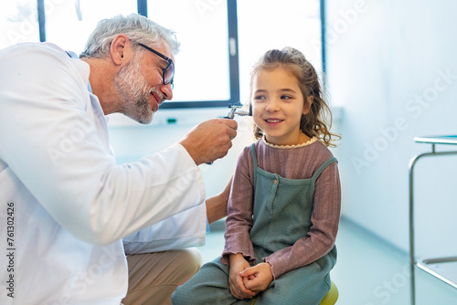Doctor examining little girl's ear using otoscope, looking for ear infection. Friendly relationship between the doctor and the child patient. photo