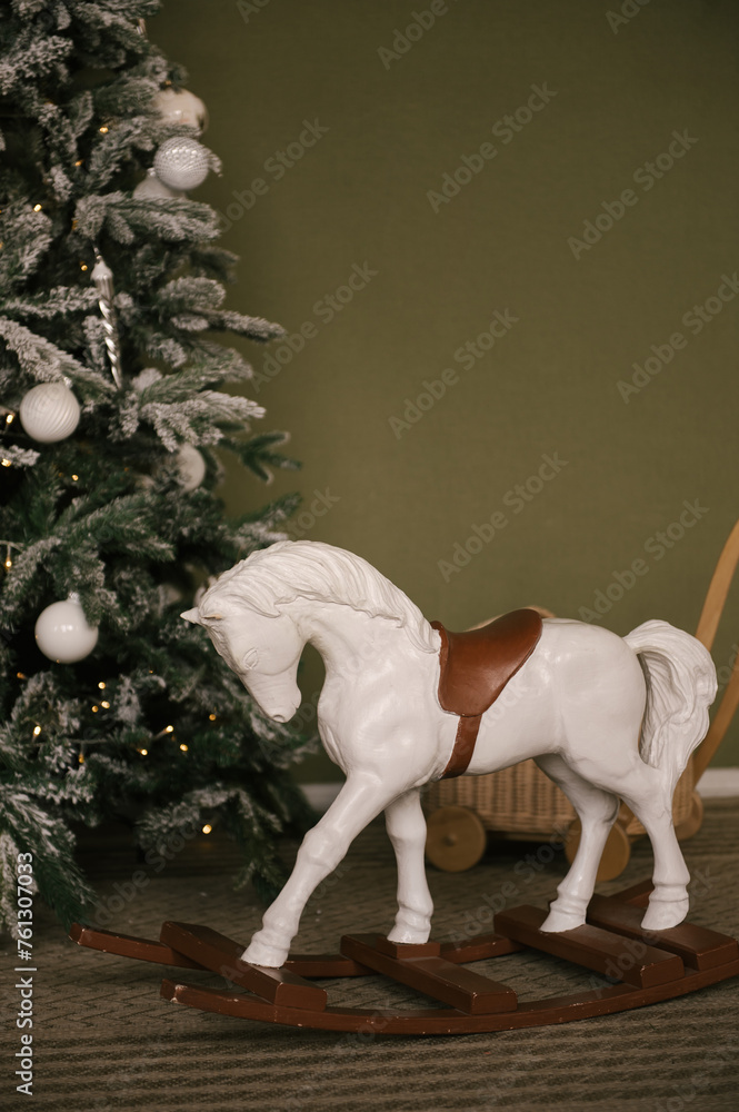 Beautiful New Year decor, a Christmas tree on the background of an olive wall and a horse made of wood