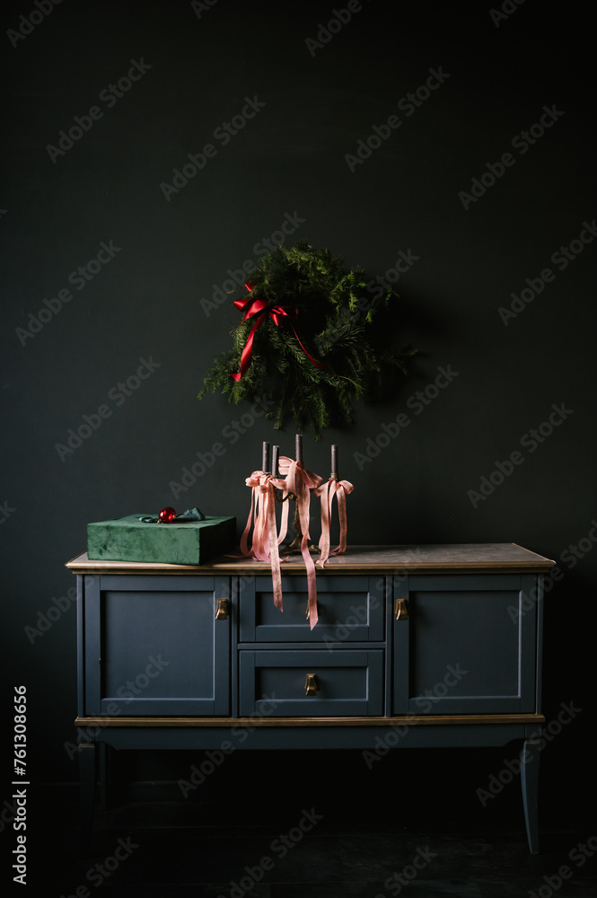 Beautiful New Year decor, a Christmas wreath on a vintage chest of drawers in a stylish dark living room interior