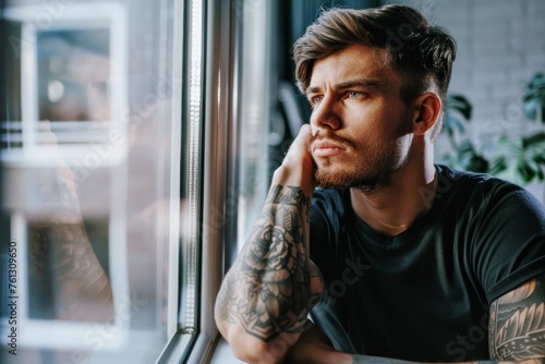 handsome young man in black t-shirt with tattoos looking through window photo