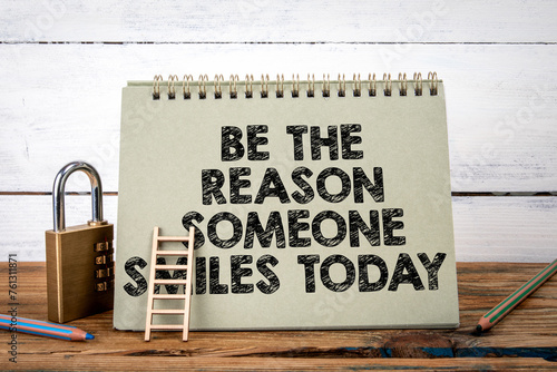 Be The Reason Someone Smiles Today. Green notepad on wooden texture table and white background photo