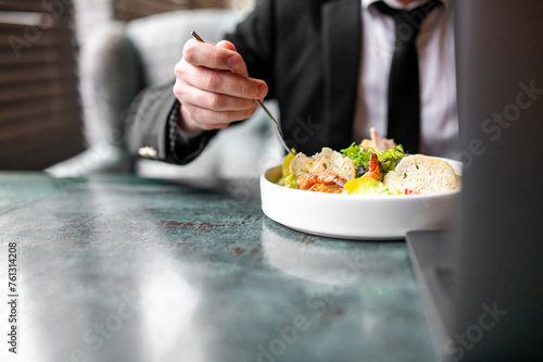 person savoring a fresh salad at a stylish green table. The individual, dressed in formal attire, uses a fork to enjoy the colorful mix of leafy greens, vegetables, and bread. photo
