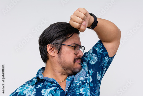 A man in a blue Hawaiian shirt, isolated on white, is humorously checking for underarm odor. Forgot to put on deodorant. photo