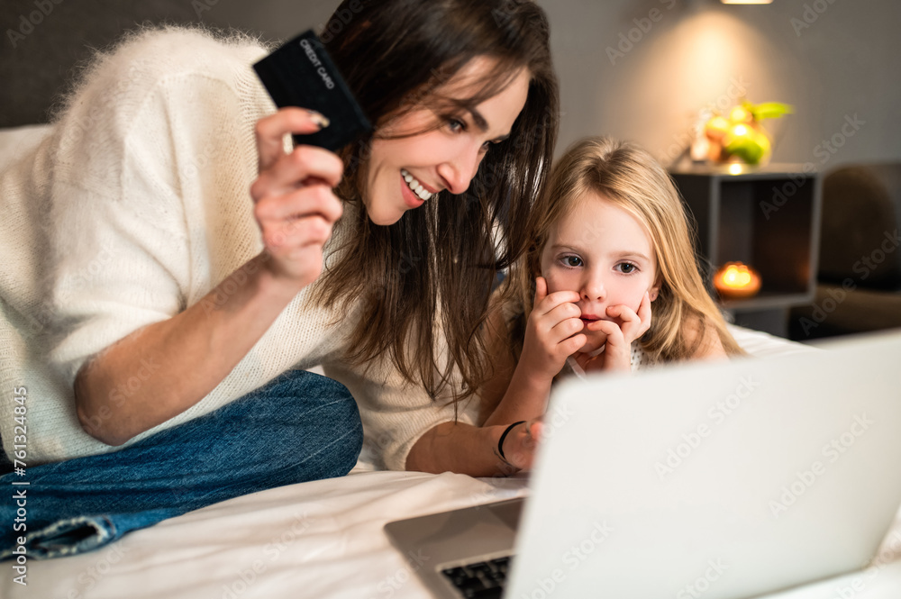 Woman and little daughter with laptop and credit card making online reservation of hotel room Woman and little daughter with laptop and credit card making online reservation of hotel room