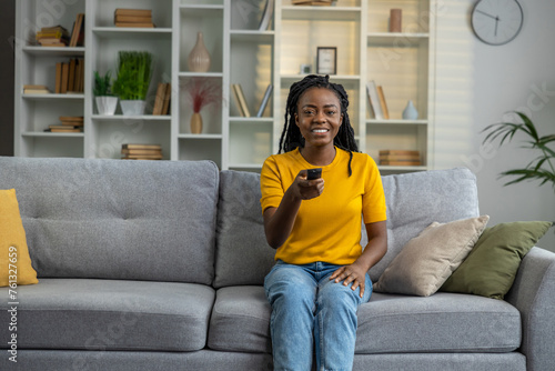 Cute dark-skinned young woman watching tv and holding control panel in hands